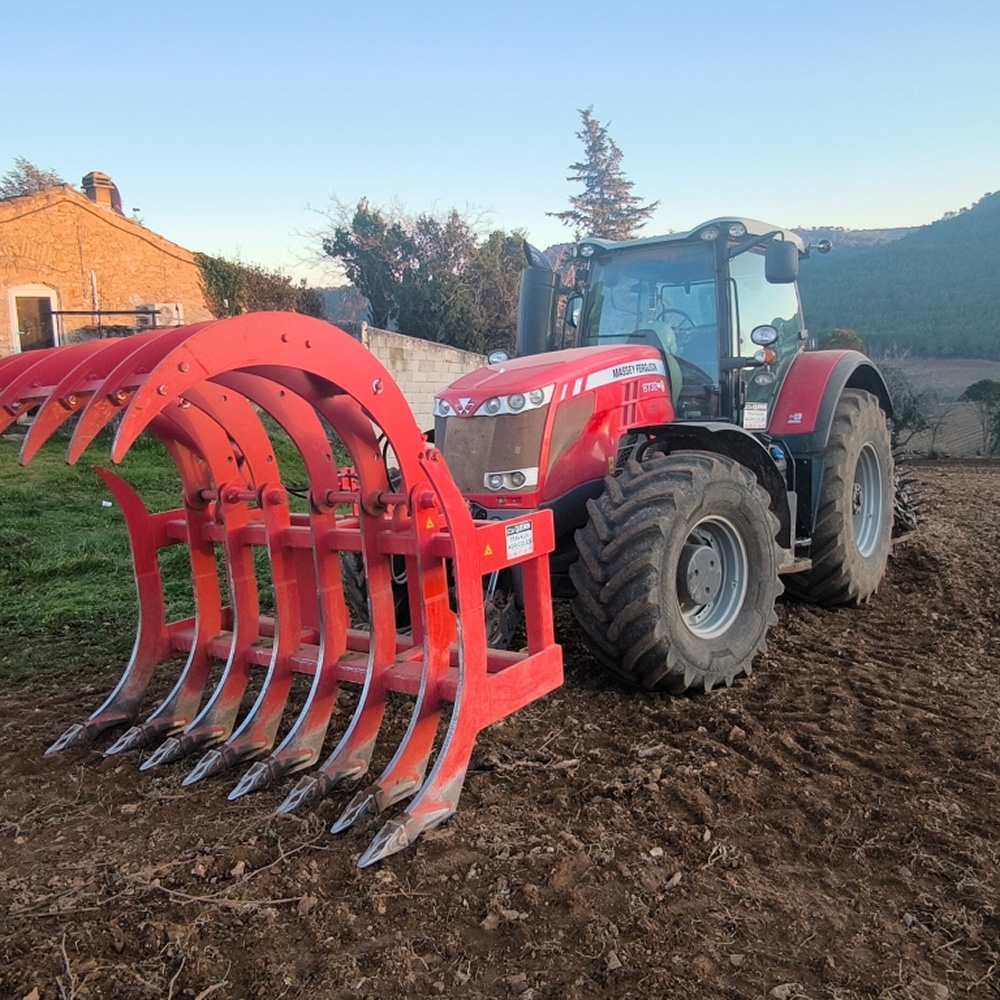 Tracteur Massey Ferguson avec pince à griffes Quivogne Tracteur Massey Ferguson rouge avec pince à griffes Quivogne dans un champ labouré sous un ciel clair.
