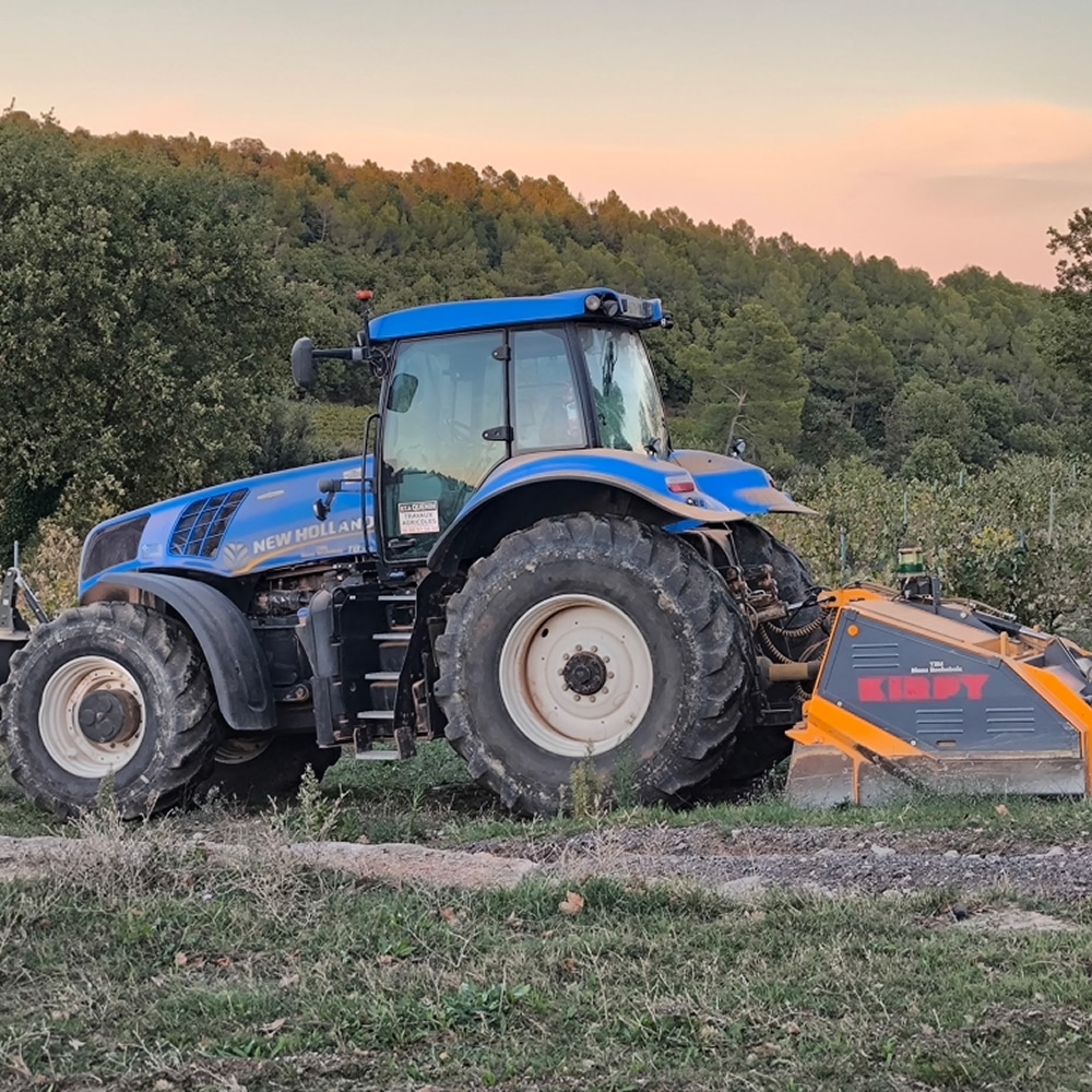 Tracteur New Holland et Matériel Kirpy en Plein Champ Tracteur New Holland bleu avec équipement Kirpy orange dans un champ agricole au coucher du soleil.