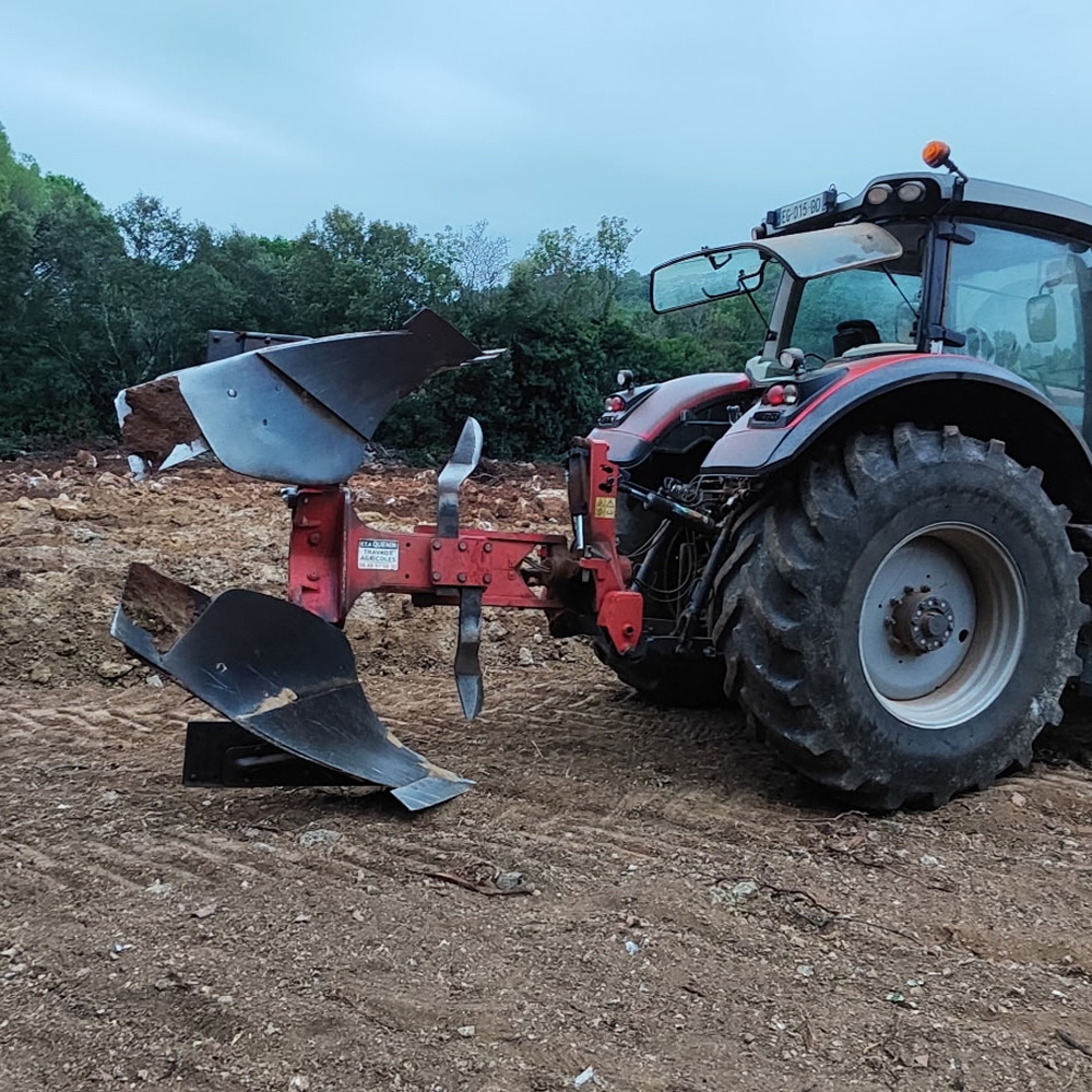 Tracteur rouge avec charrue réversible pour labour Tracteur rouge équipé d'une charrue réversible Quenin sur un terrain de labour sous un ciel nuageux.